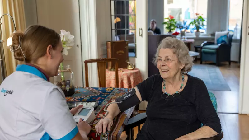 Medewerker van KleinGeluk meet de bloeddruk bij een oudere dame thuis