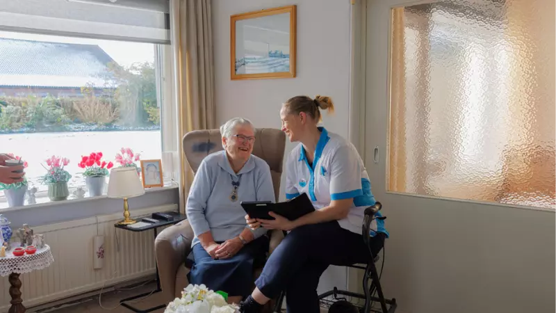 Medewerker van KleinGeluk zit bij een bewoner van een woning van Thuiszorg Avondzon. Zij hebben onderonsje.