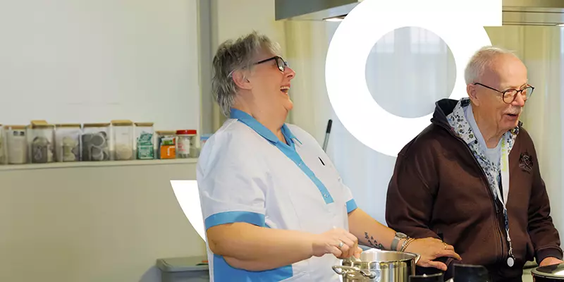 Medewerker van KleinGeluk is aan het koken met een bewoner. Zij zijn hierbij allebei aan het lachen.
