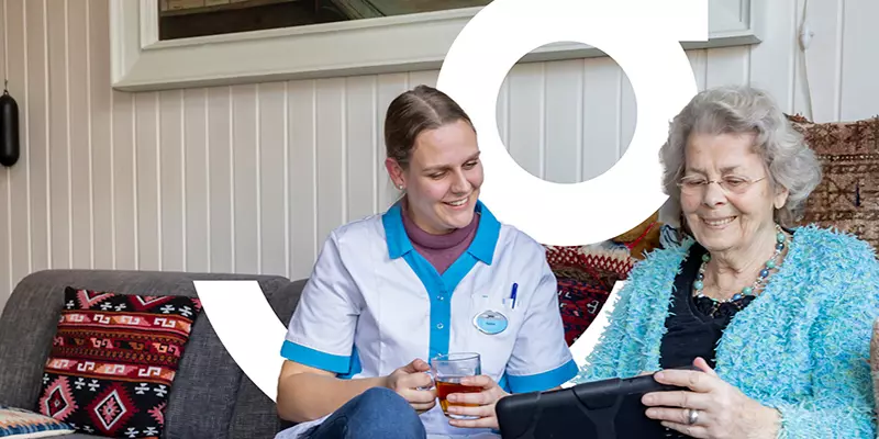 Oudere mevrouw laat thuiszorgmedewerkster van KleinGeluk wat zien op haar tablet