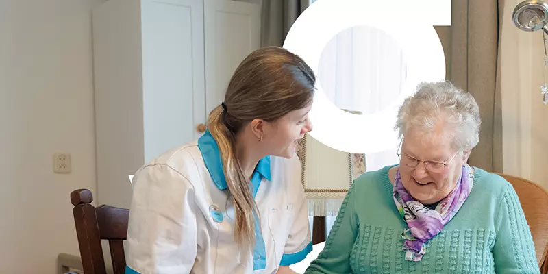 Stagiaire is in gesprek met een oudere mevrouw over haar leven van vroeger. Ze bladeren samen door een fotoalbum.