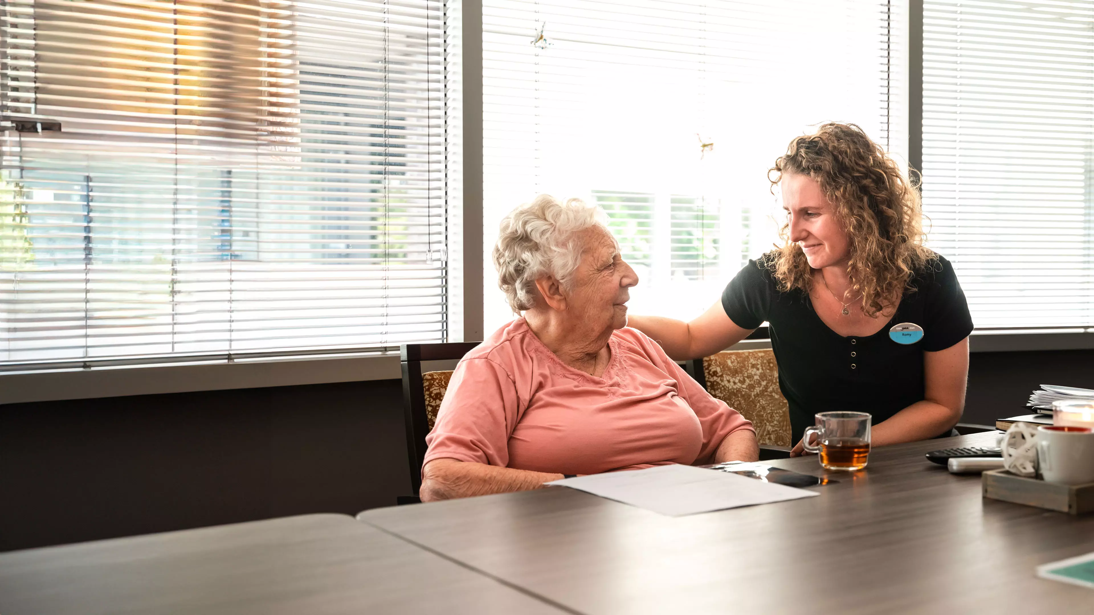 Medewerker Welzijn zit met een bewoner op de gang.